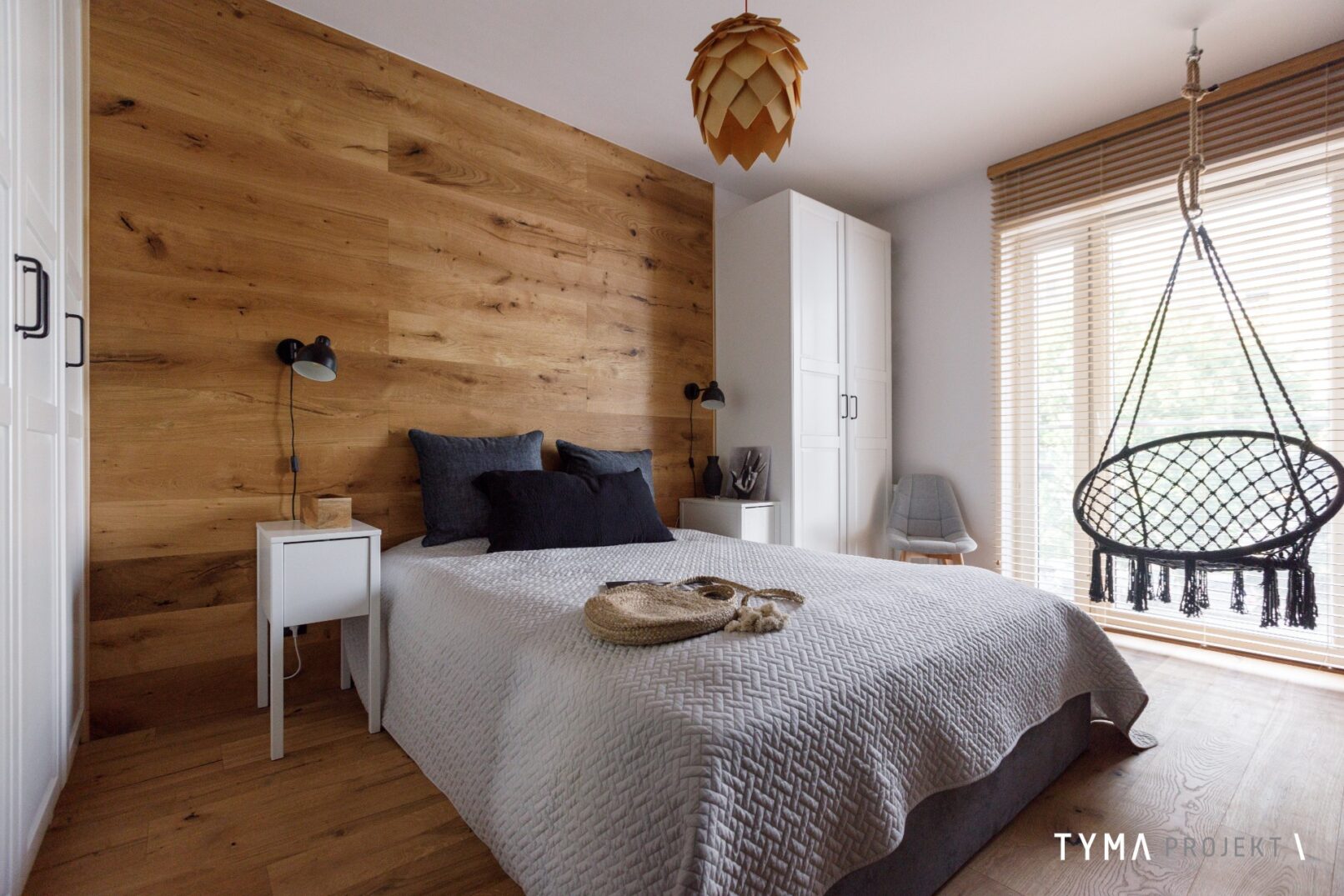 Sypialnia z podwieszanym fotelem. Ściana obłożona drewnem.