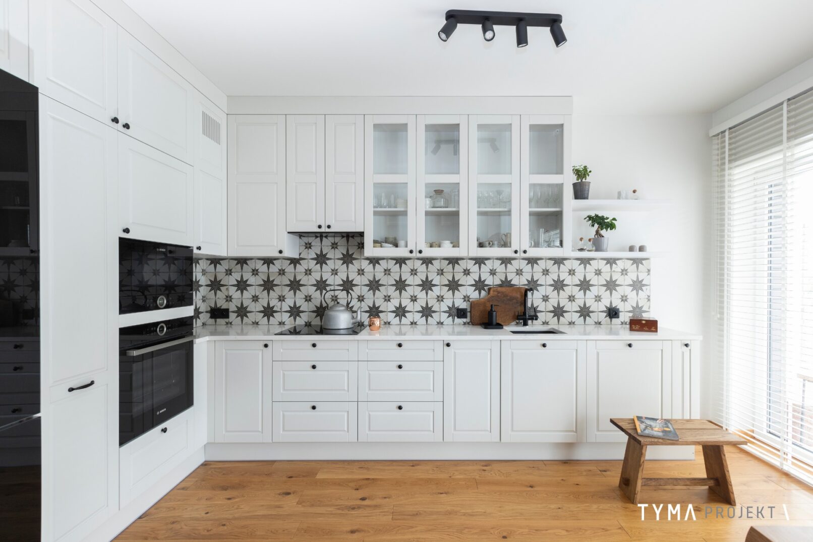 Białe fronty, wzorzyste płytki, blat z konglomeratu.