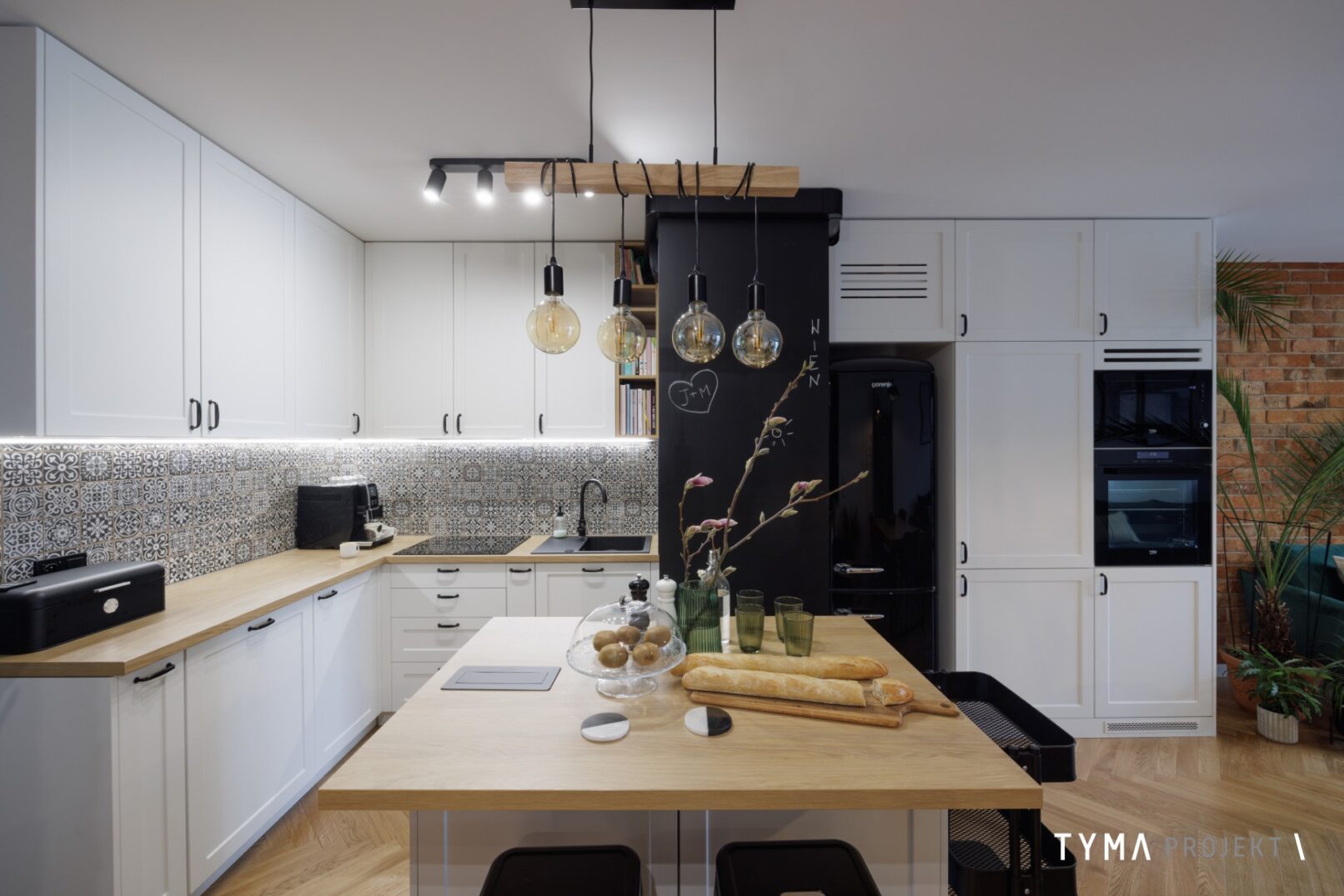 Kuchnia z wyspą. Lodówka retro i wyraźny dekor nad blatem.